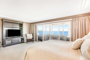 Habitación de hotel con una cama grande, un televisor de pantalla plana, un área de descanso con vistas al mar y un balcón.