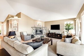 A living room with a fireplace, sofas, a coffee table, and a TV. - 3 BR Waterfront Retreat with Private Beach Access and Stunning Ocean Views (Freeland)