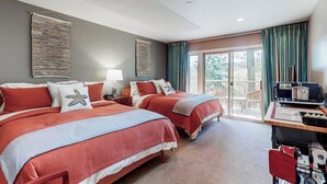 Quarto de hotel com duas camas, uma mesa com computador, janela com cortinas e varanda.