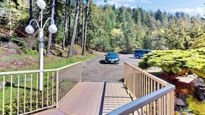 Um deck de madeira com guarda-corpo, um caminho que leva a um carro e uma área arborizada ao fundo.