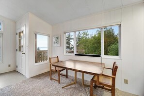 A room with a wooden dining table and chairs, a large window with a view of greenery, and a door leading outside. - Spacious 3 Bedroom Greenbank Home with Beach Access and Game Room (Greenbank)