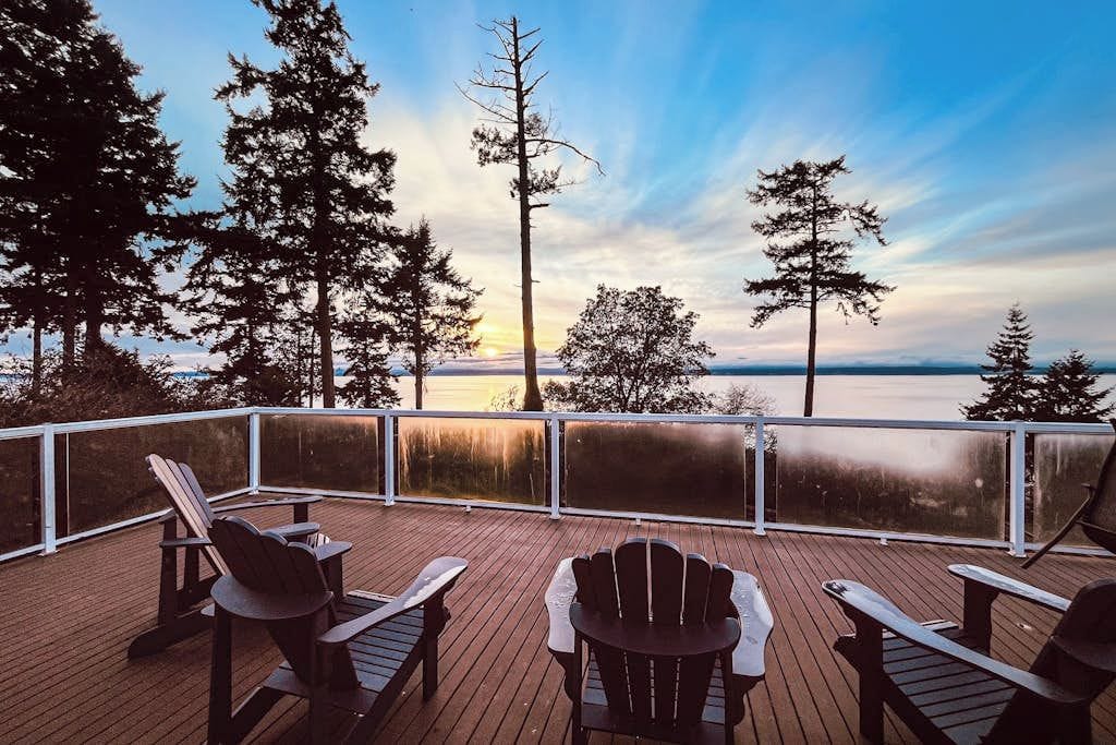 A deck with Adirondack chairs overlooking a body of water and trees.
