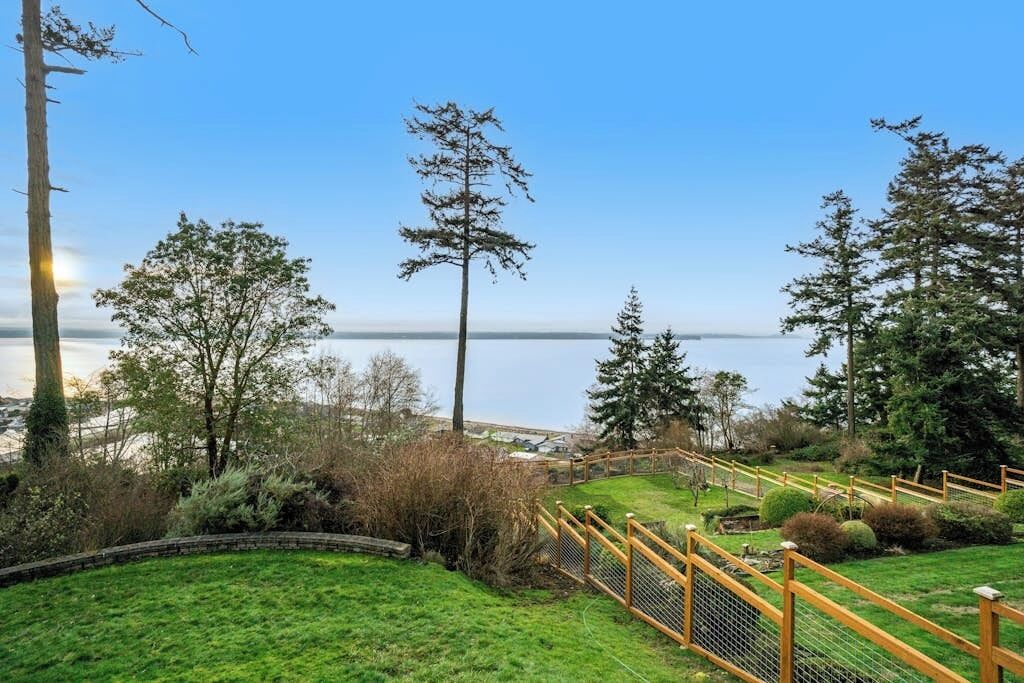 A grassy area with a wooden fence, trees, and a clear sky.