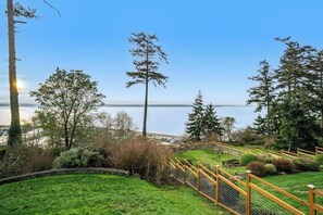 A grassy area with a wooden fence, trees, and a clear sky. - Spacious 3 Bedroom Greenbank Home with Beach Access and Game Room (Greenbank)