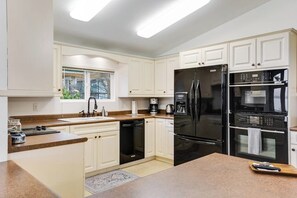 A modern kitchen with white cabinetry, a black refrigerator, and a built-in oven. - Spacious 3 Bedroom Greenbank Home with Beach Access and Game Room (Greenbank)
