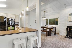 Een moderne keuken met witte kasten, een houten aanrecht en een eethoek met een tafel en stoelen.