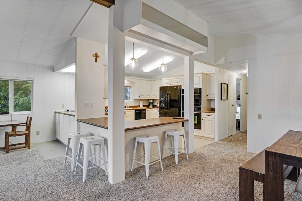 Una cocina amplia con una isla central, armarios blancos y una zona de comedor con mesa de madera y taburetes de bar.