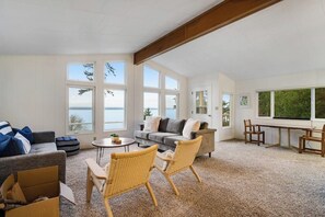 A spacious living room with a large window, a sofa, a coffee table, and wicker chairs. - Spacious 3 Bedroom Greenbank Home with Beach Access and Game Room (Greenbank)