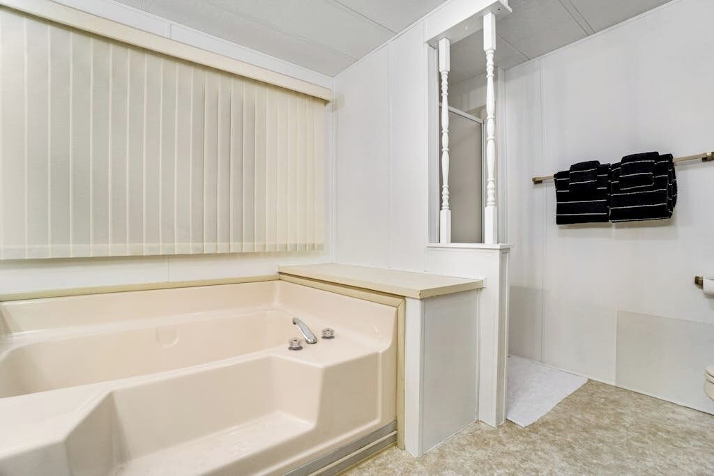 A bathroom with a bathtub, a window with blinds, and a towel rack with folded towels.