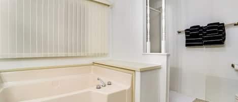 Casa de banho com banheira, janela com persianas e um porta-toalhas com toalhas dobradas.