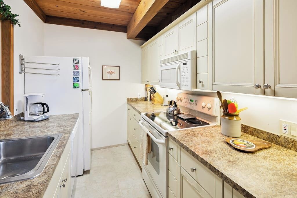 Una cocina con armarios blancos, microondas, hervidor de agua y cafetera.