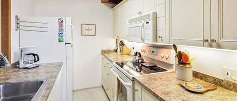 Una cocina con armarios blancos, microondas, hervidor de agua y cafetera.