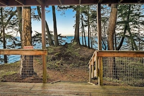 A wooden deck with a 'DANGER' sign, overlooking a forested area and a body of water.