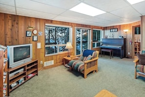 A cozy living room with a television, piano, and large windows.