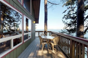 Une terrasse avec une table et des chaises, donnant sur une étendue d’eau bordée d’arbres.