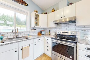 Een moderne keuken met witte kastjes, een roestvrijstalen oven en een raam met uitzicht op een zwembad.