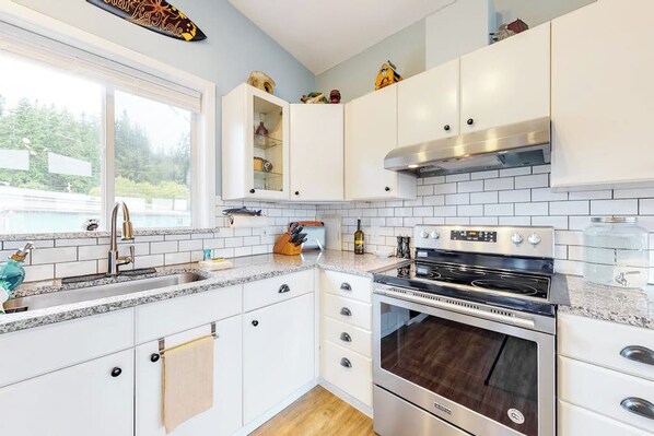 Una cocina moderna con armarios blancos, un horno de acero inoxidable y ventana con vistas a una piscina.