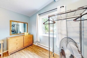 Een slaapkamer met een houten dressoir, een spiegel, een ventilator en een raam met gordijnen.