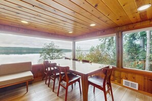 Ein Zimmer mit Holzwänden, einem großen Tisch mit Stühlen, einer Bank und Blick auf einen See.