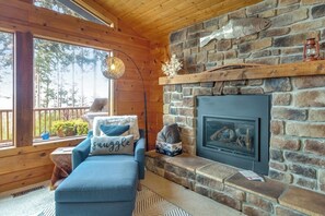A cozy cabin interior with a stone fireplace, a blue sofa with a pillow, and a wooden ceiling. - Family friendly, Two-Story Retreat with Deck, grill and Ocean Views (Coupeville)