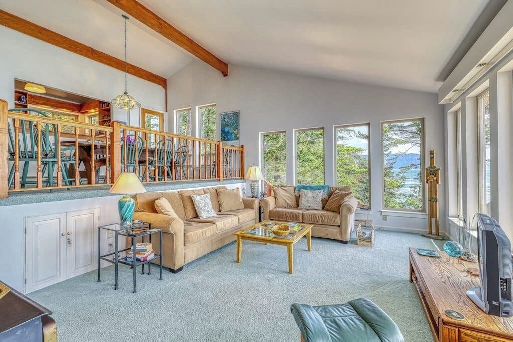 A spacious living room with a high ceiling, built-in bookshelves, a large window with a view, and a cozy seating area.