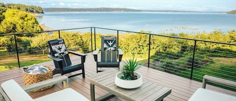 Een terras met buitenmeubilair, een potplant en uitzicht op een wateroppervlak.
