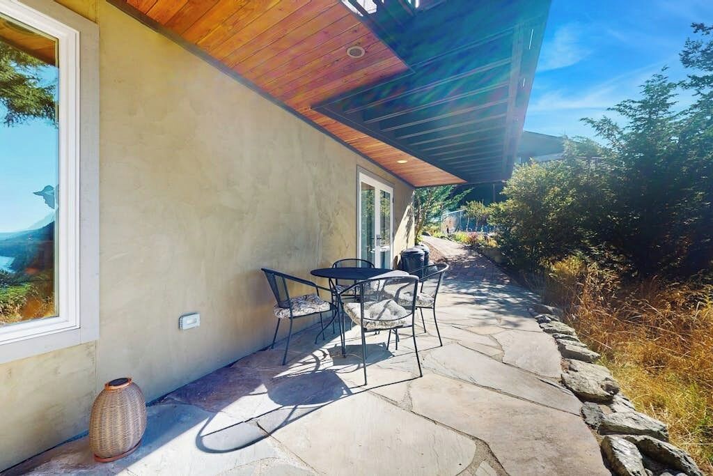 Une terrasse avec un sol en pierre, une table et des chaises, et une grande fenêtre donnant sur un paysage.