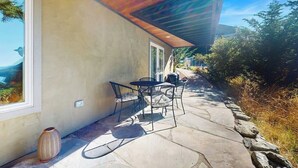 Een terras met stenen vloer, een tafel en stoelen, en een groot raam met uitzicht op het landschap.