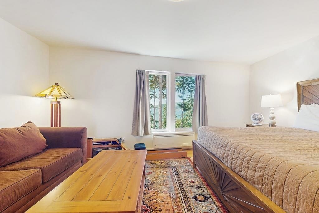 Une chambre d’hôtel avec un lit, un canapé, une table en bois, une lampe et une fenêtre avec des rideaux.