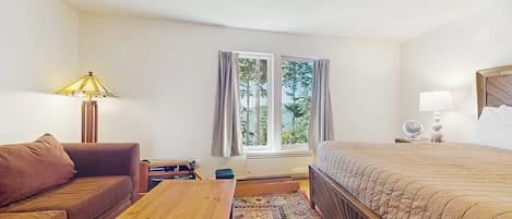 A hotel room with a bed, a sofa, a wooden table, a lamp, and a window with curtains.