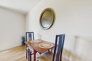 A dining area with a wooden table, two woven placemats, and a decorative plate on the wall.