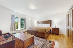 A bedroom with a wooden bed, bedside tables, a desk, and a large window.