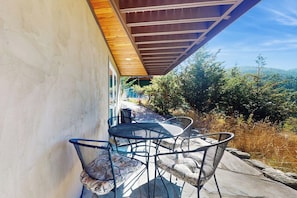 Une terrasse extérieure avec une table et des chaises, un plafond en bois et une vue sur les arbres et les collines.