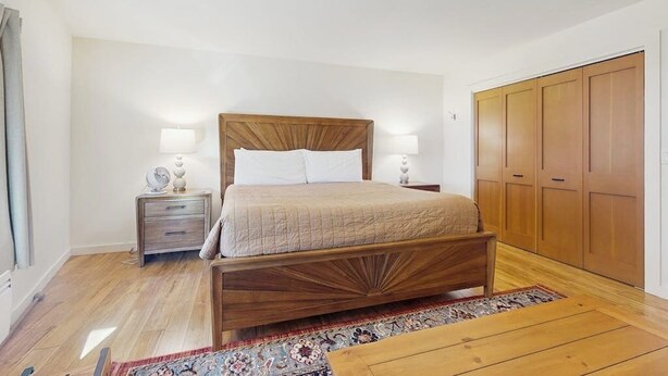 A bedroom with a wooden bed, bedside tables, a nightstand, a wardrobe, and a patterned rug.