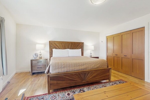 A bedroom with a wooden bed, bedside tables, a nightstand, a wardrobe, and a patterned rug.