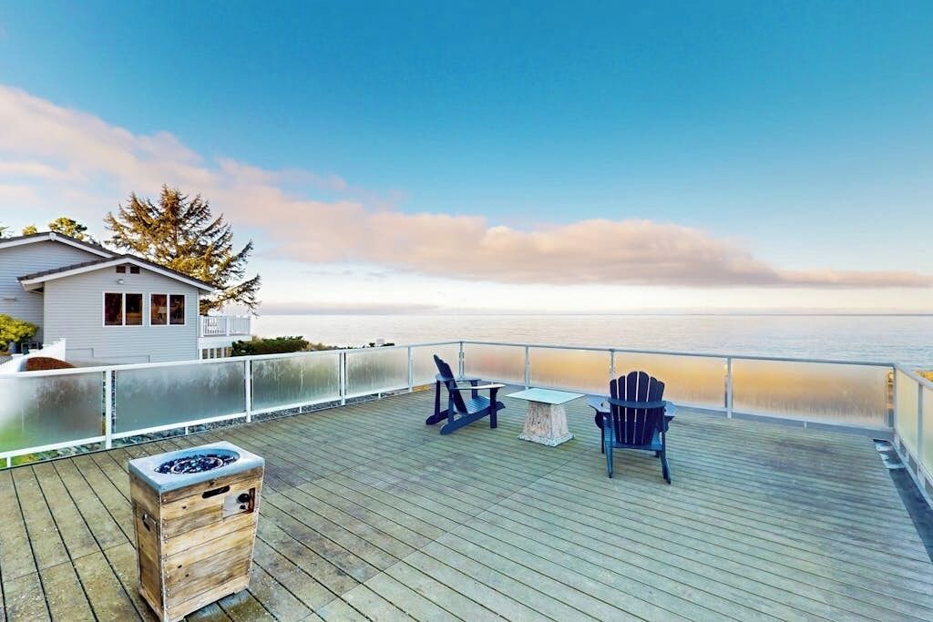 Une terrasse en bois avec vue sur l’océan, une petite table et deux chaises.