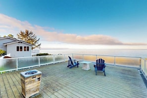 A wooden deck with a view of the ocean, a small table, and two chairs.