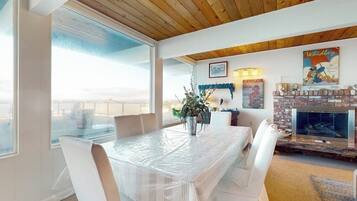 A dining area with a covered table, chairs, a fireplace, and a large window.