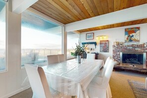 A dining area with a covered table, chairs, a fireplace, and a large window.