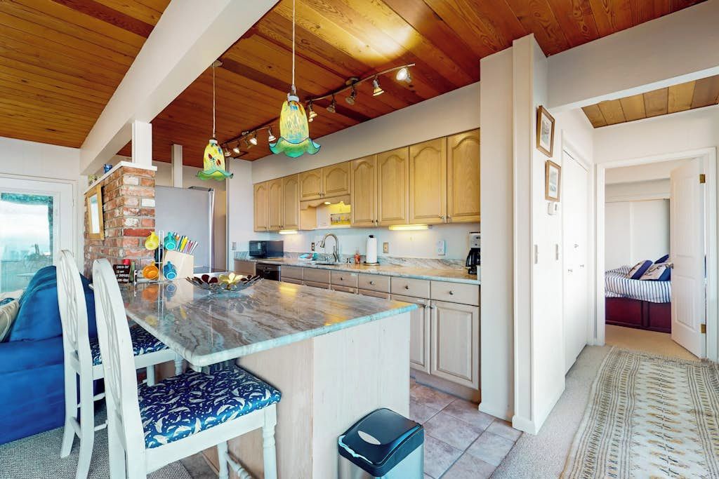 Une cuisine moderne avec des meubles en bois, un plan de travail en marbre et des luminaires suspendus.