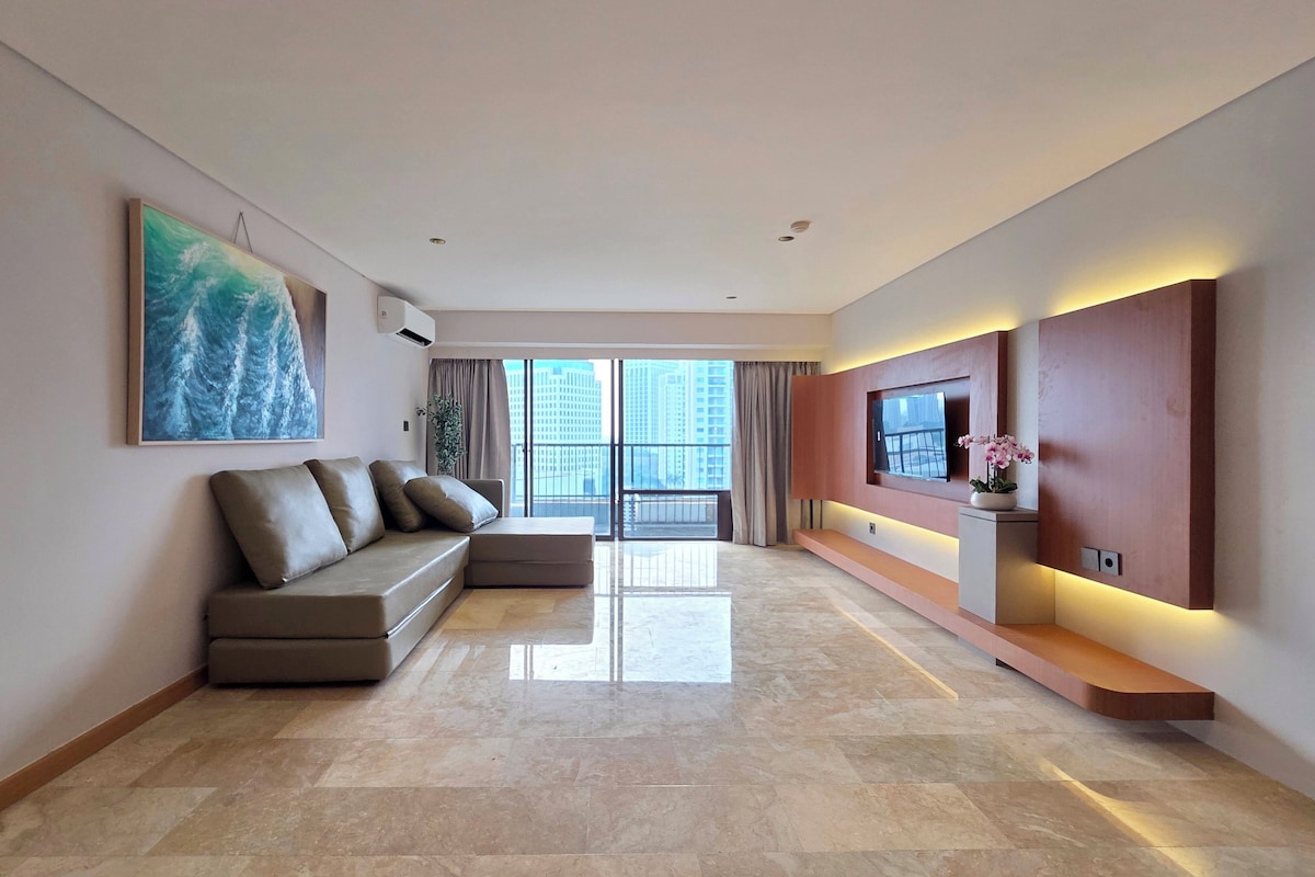 A modern living room with a sectional sofa, a flat-screen TV, and a large window with a city view.