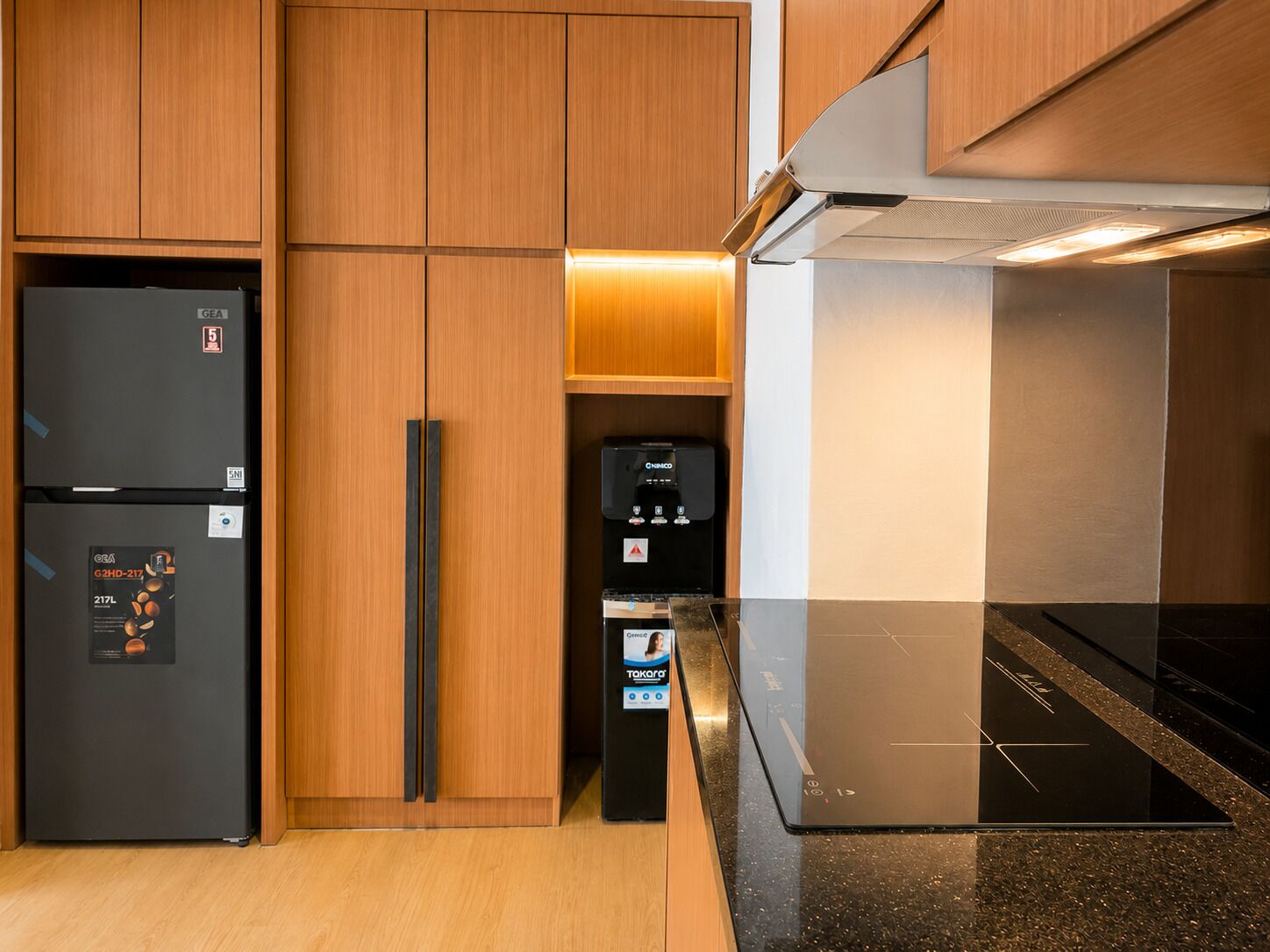 A kitchen with wooden cabinets, a black refrigerator, a coffee machine, and a black induction cooktop.