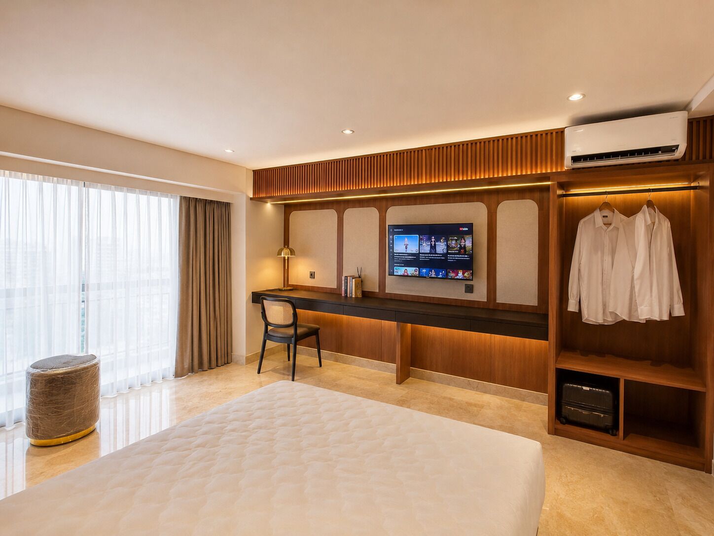 Habitación de hotel con cama, escritorio, televisor, armario y ventana con cortinas.