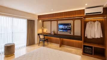 A hotel room with a bed, a desk, a TV, a wardrobe, and a window with curtains.
