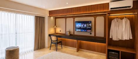 Habitación de hotel con cama, escritorio, televisor, armario y ventana con cortinas.