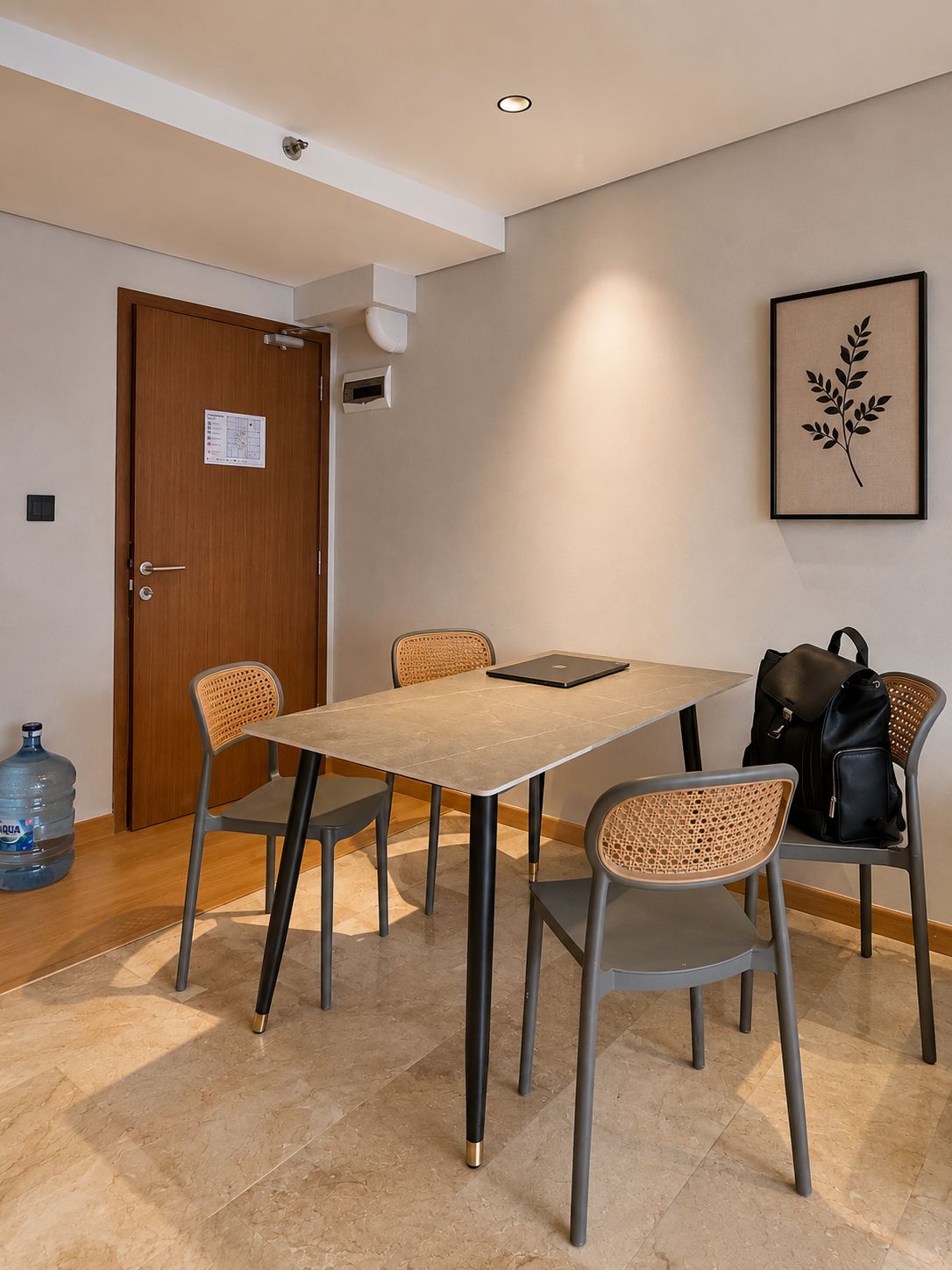 A conference room with a rectangular table, four chairs, a laptop, a water dispenser, and a framed plant on the wall.