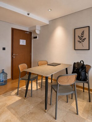 A conference room with a rectangular table, four chairs, a laptop, a water dispenser, and a framed plant on the wall. - Solana ONE By SanLiving - Senayan (Jakarta)
