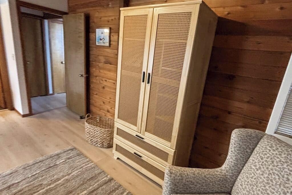 A wooden wardrobe with two doors, a woven basket, a leopard print chair, and a wooden floor.