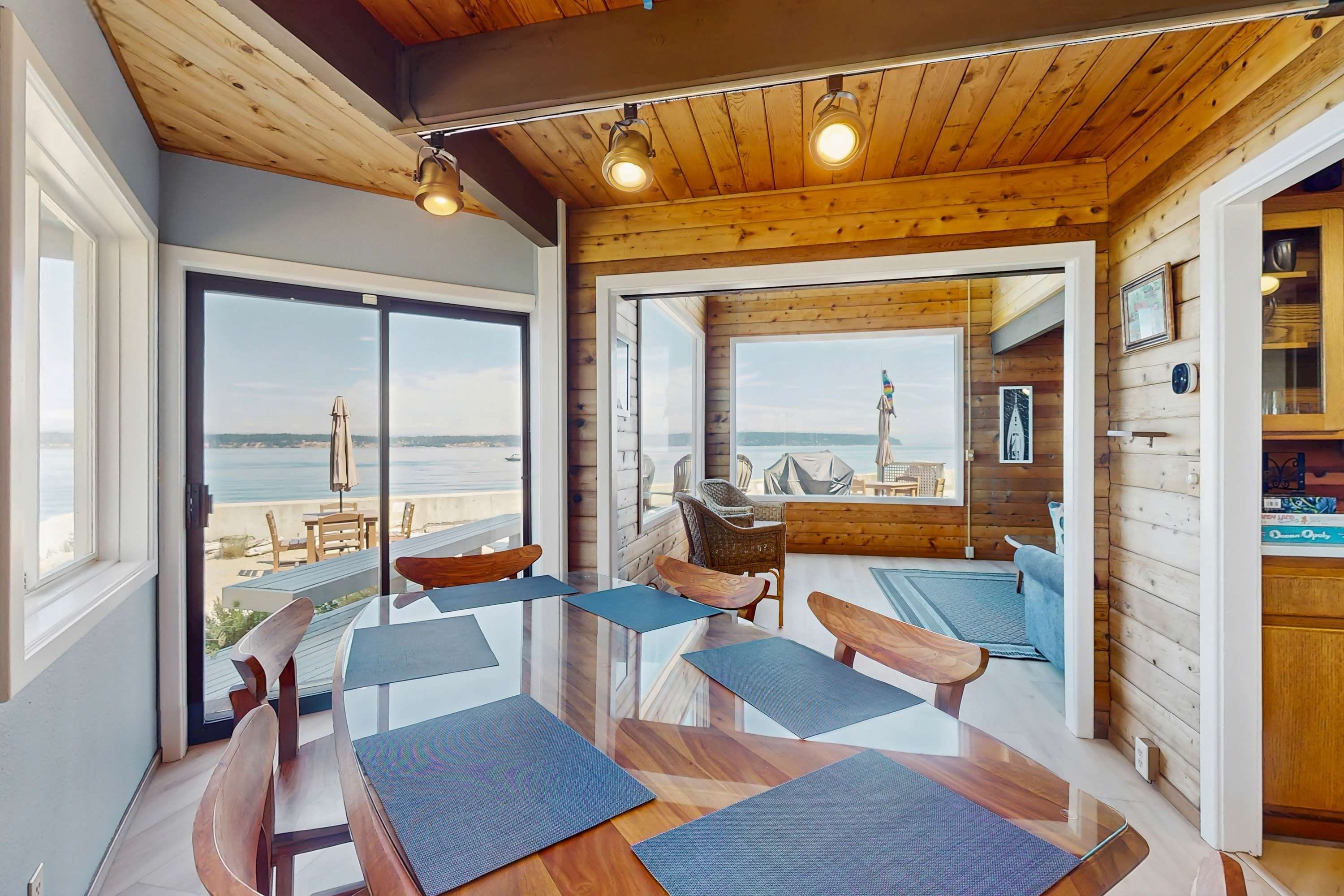 A modern interior with a glass dining table, wooden chairs, and a view of the beach.