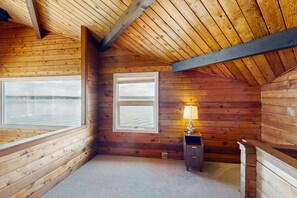 A cabin with wooden walls, a sloped ceiling, two windows, a lamp, and a small wooden cabinet. - Stunning Waterfront Home with Beach Access & Whale Watching (Langley)